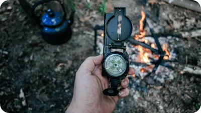 man holding a compass next to a bushcraft campsite