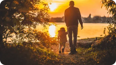 man walking with his young daughter beside a scenic lake at sunset