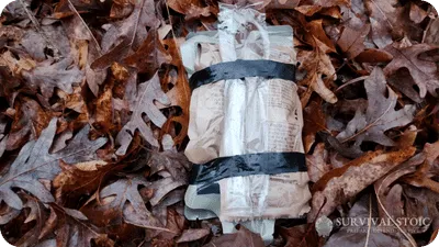 Blake's MRE broken down into critical items wrapped in tape and laying on the ground in the leaves