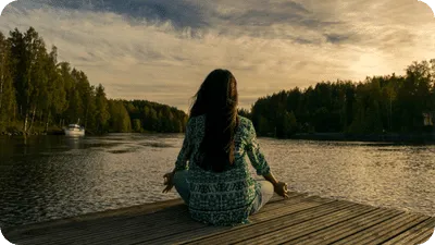 Meditating woman sitting on a dock looking out over a lake during sunset