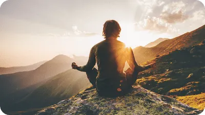 Man meditating outside in the mountains during sunset