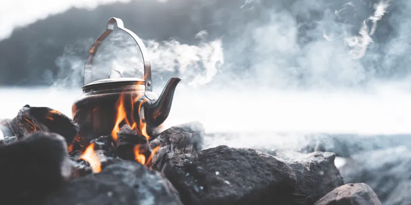 Boiling water in red pot pan on top of stove flames with smokes