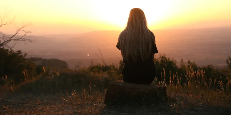 What is a Stoic Person?
Woman sitting on a hill looking at the sun setting over a mountain