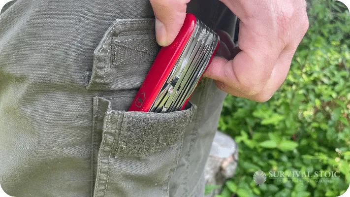 The author's putting a Swiss Army knife into one of the pockets in his bushcraft pants