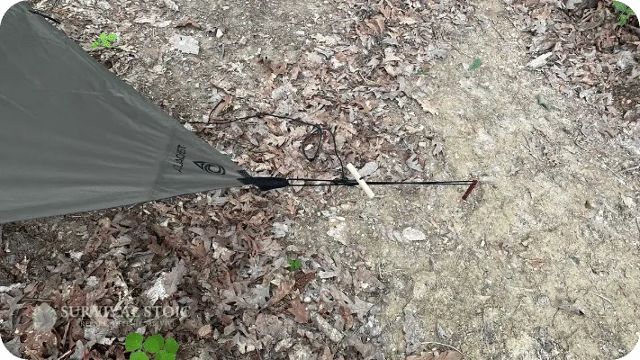 Best Tent Stakes for Bushcraft, shown holding a bushcraft and Survival Tarp pitched in the woods