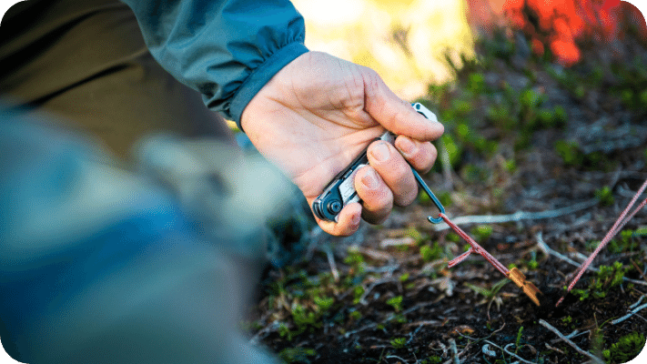 A man at a campsite pulling a tent stake out of the ground with the Gerber Stake out multitool